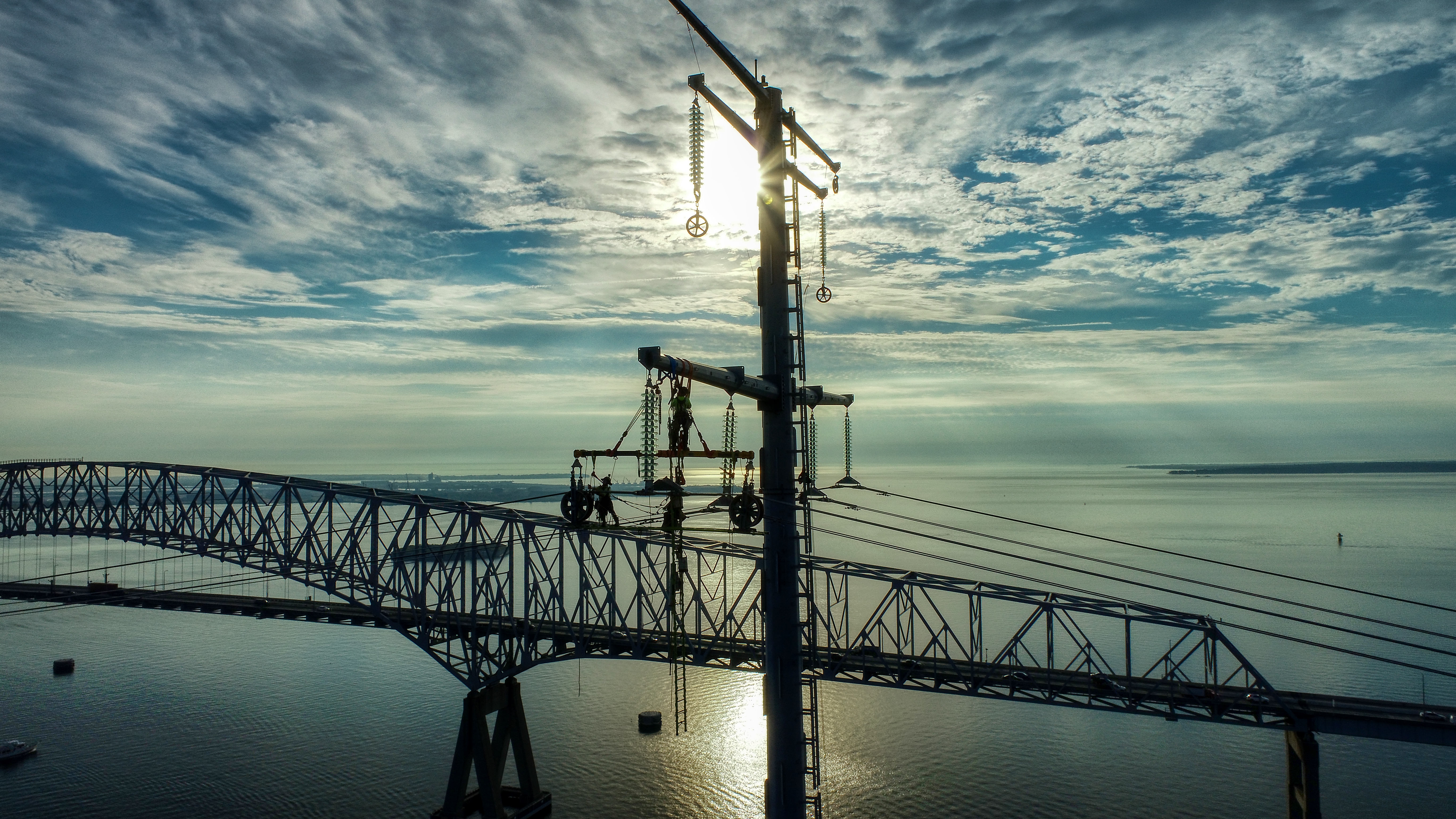 Aerial view of transmission line workers on a tower beside the Chesapeake Bay Bridge at sunrise
